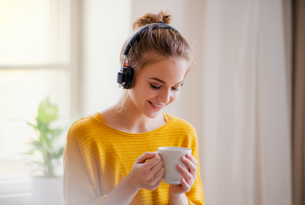 A young happy college female student sitting at the table at home, using headphones when studying.