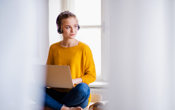 A young female student sitting on the desk, using headphones when studying. Copy space.