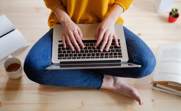 A midsection of young female student sitting on floor using laptop when studying, top view.