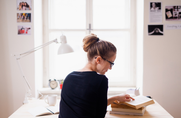 A rear view of young female student sitting at the table, studying.