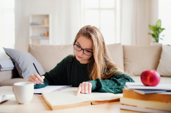 A young unhappy and sad college female student sitting at the table at home, studying.