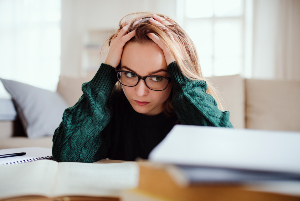 A young unhappy and sad college female student sitting at the table at home, studying.