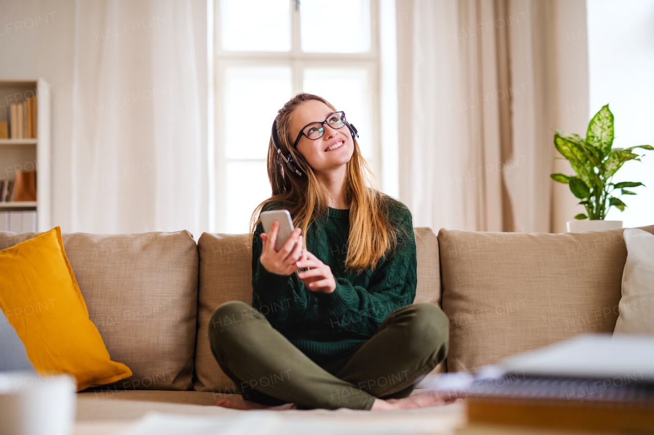 A young happy college female student sitting at the table at home, using headphones when studying.