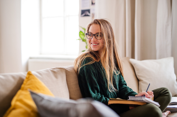 A happy young female student sitting on sofa, studying. Copy space.