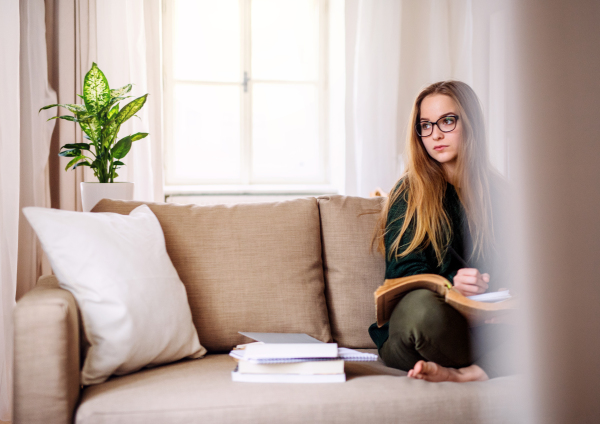 A happy young female student sitting on sofa, studying. Copy space.