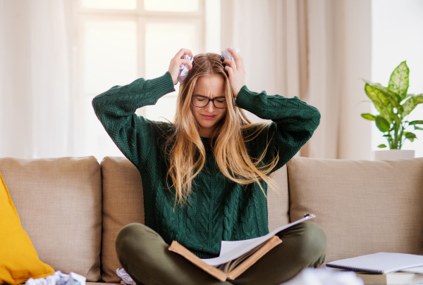 An unhappy, sad and frustrated female student sitting on sofa, studying.