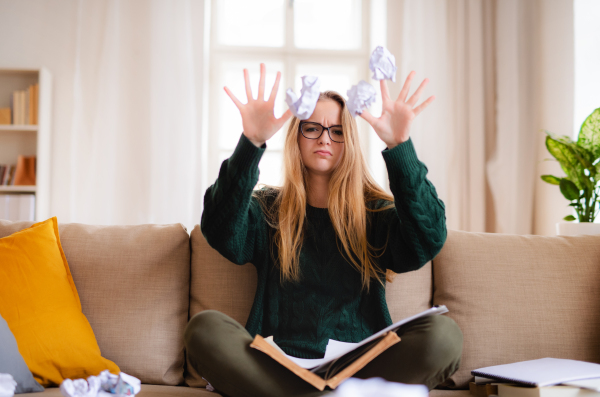 An unhappy, sad and frustrated female student sitting on sofa, studying.