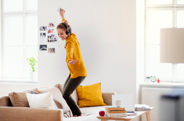 A young female student with headphones and telephone having a break when studying, dancing on sofa.