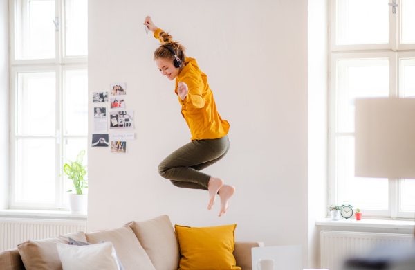 A young female student with headphones and telephone having a break when studying, jumping on sofa.