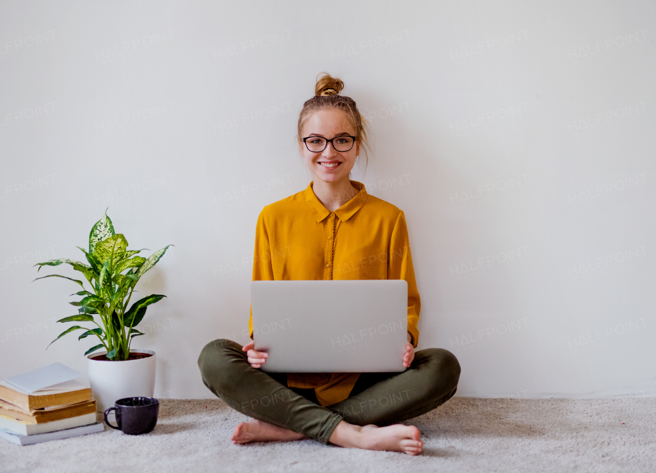 A young college female student sitting on floor at home, using laptop when studying.