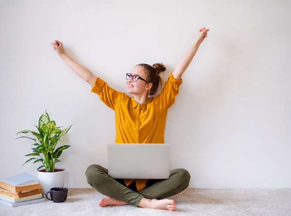 A young happy college female student sitting on floor at home, using laptop when studying.