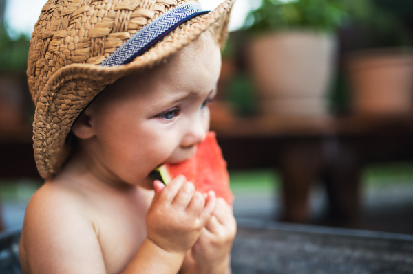 A happy small girl in bath tub outdoors in garden in summer, eating watermelon.