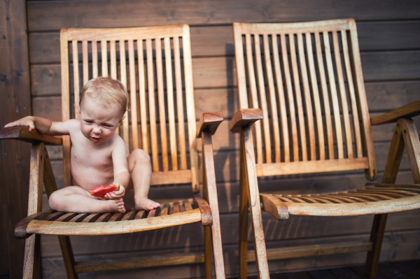 Small girl sitting on wooden chair on a patio in summer, eating watermelon. Copy space.