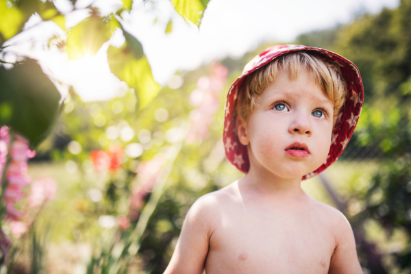 A small boy with a hat standing outdoors topless in garden in summer. Copy space.