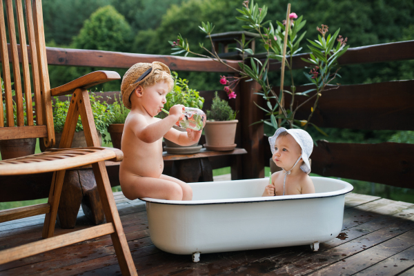 Small children with a drink sitting in bath outdoors in garden in summer, playing in water.