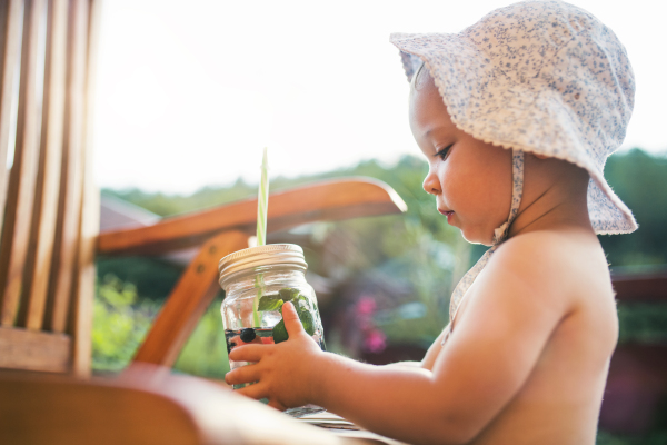 A small girl with a drink with fruit standing by a table on a patio in summer.