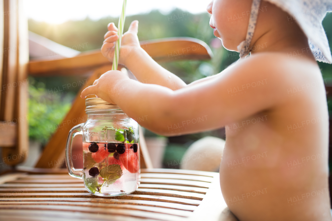 A midsection of unrecognizable small girl with a drink standing by a table on a patio in summer.