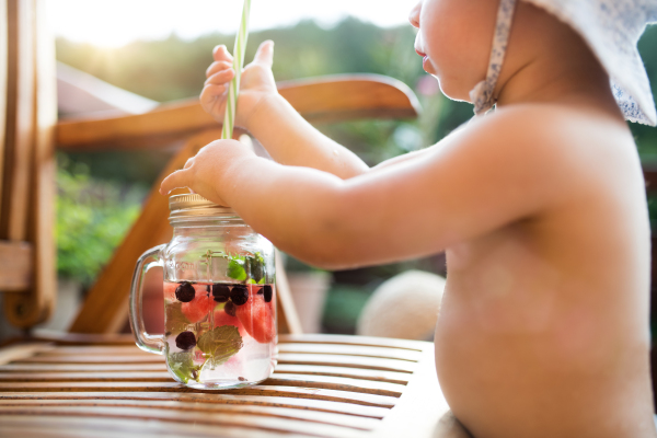 A midsection of unrecognizable small girl with a drink standing by a table on a patio in summer.