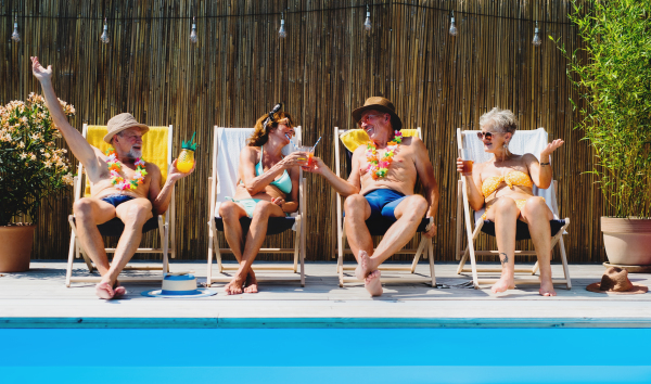 Group of cheerful seniors sitting by swimming pool outdoors in backyard, relaxing.