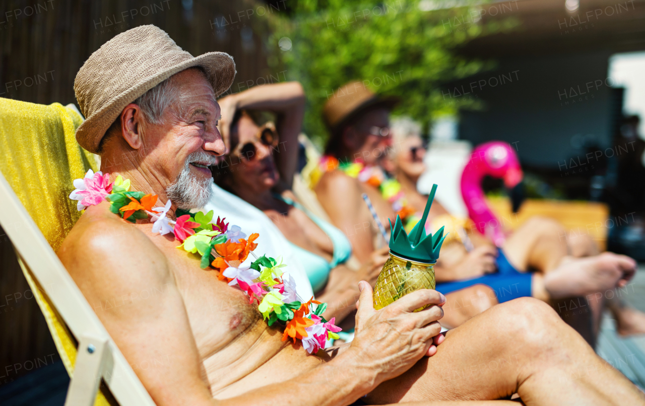 Group of cheerful seniors sitting by swimming pool outdoors in backyard, a party concept.