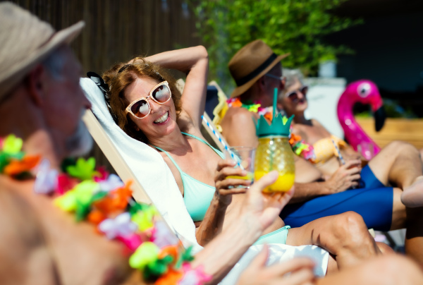 Group of cheerful seniors sitting by swimming pool outdoors in backyard, a party concept.