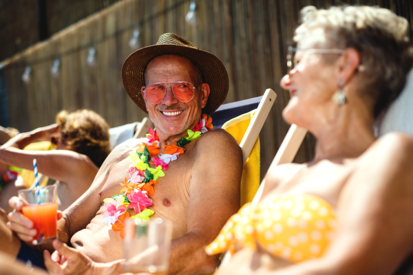 Group of cheerful seniors sitting by swimming pool outdoors in backyard, a party concept.