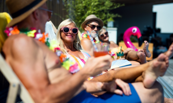 Group of cheerful seniors sitting by swimming pool outdoors in backyard, a party concept.