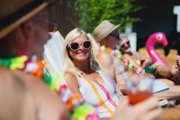 Group of cheerful seniors sitting by swimming pool outdoors in backyard, a party concept.