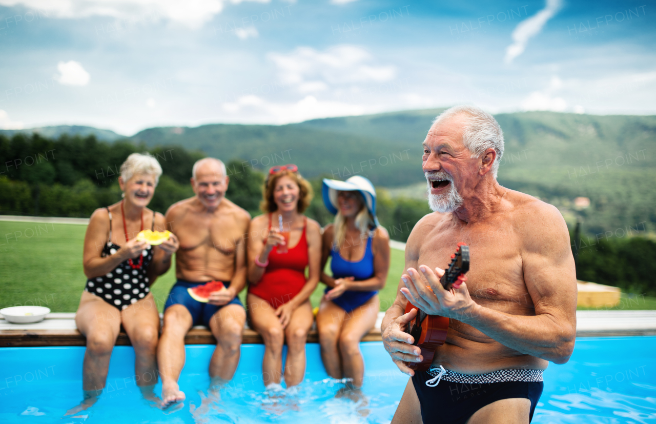 Group of cheerful seniors with guitar by swimming pool outdoors in backyard, a party concept.