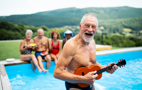 Group of cheerful seniors with guitar by swimming pool outdoors in backyard, a party concept.