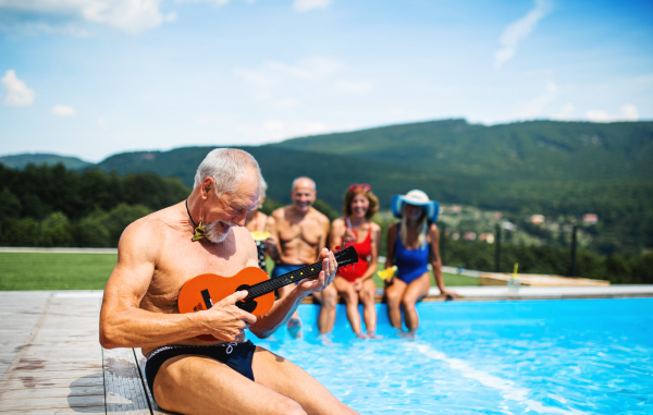 Group of cheerful seniors with guitar by swimming pool outdoors in backyard, a party concept.