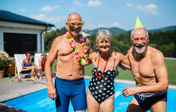 Group of cheerful seniors by swimming pool outdoors in backyard, a party concept.