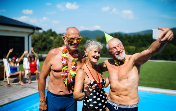 Group of cheerful seniors taking selfie by swimming pool outdoors in backyard, a party concept.