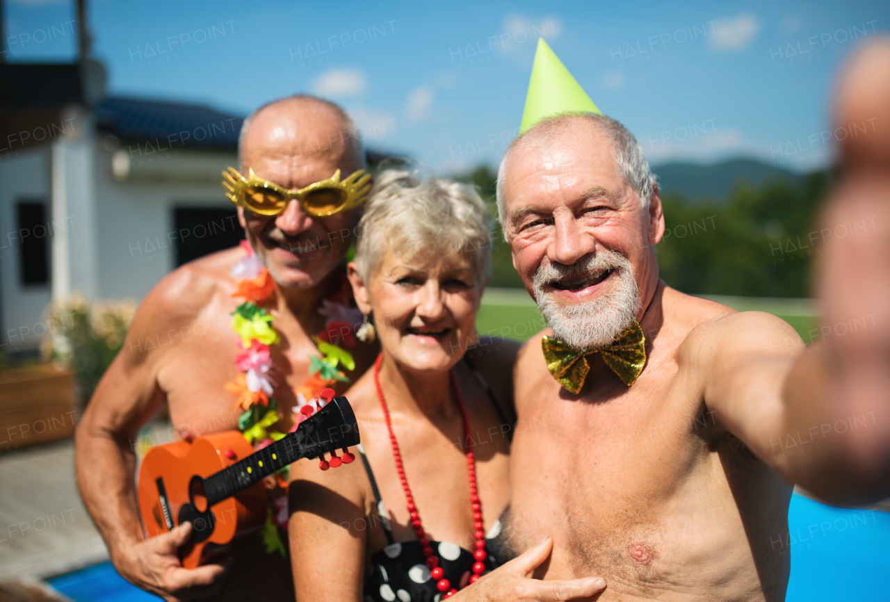 Group of cheerful seniors taking selfie by swimming pool outdoors in backyard, a party concept.