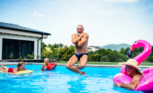 Group of cheerful seniors in swimming pool outdoors in backyard, jumping in water.