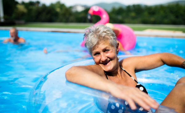 Portrait of senior woman in swimming pool outdoors in backyard, looking at camera. Copy space.