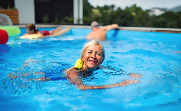 Portrait of senior woman in swimming pool outdoors in backyard, looking at camera. Copy space.