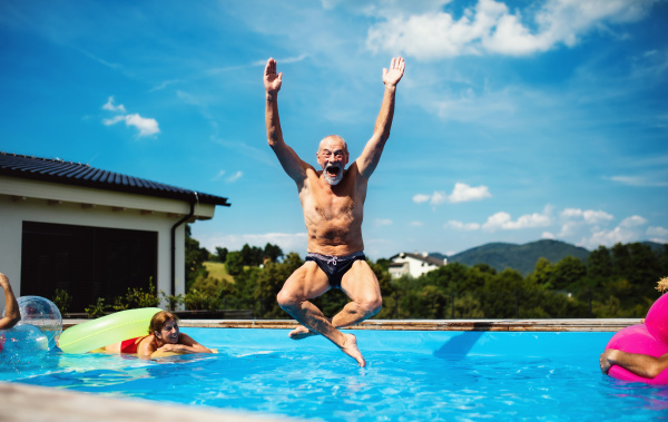 Group of cheerful seniors in swimming pool outdoors in backyard, jumping in water.