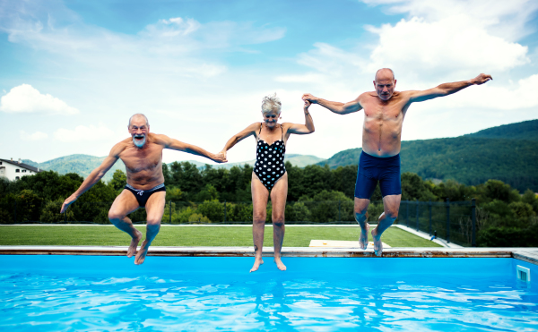 Group of cheerful seniors in swimming pool outdoors in backyard, jumping in water.