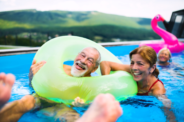 A group of cheerful seniors in swimming pool outdoors in backyard, having fun.