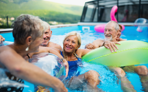 Group of cheerful seniors in swimming pool outdoors in backyard, talking and having fun.