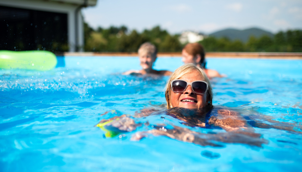 Portrait of senior woman with friends in swimming pool outdoors in backyard.