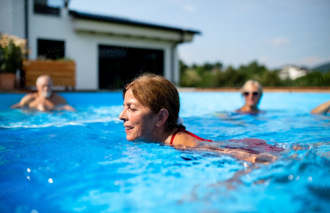 Portrait of senior woman with friends in swimming pool outdoors in backyard.