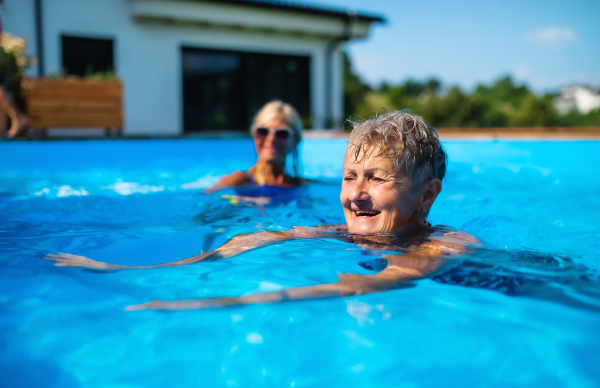 Portrait of senior woman with friends in swimming pool outdoors in backyard.