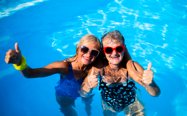 High angle view of cheerful senior women in swimming pool outdoors in backyard, looking at camera.