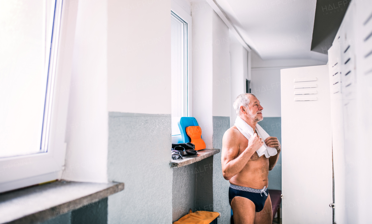 Senior man standing by the lockers in an indoor swimming pool. Active pensioner enjoying sport.