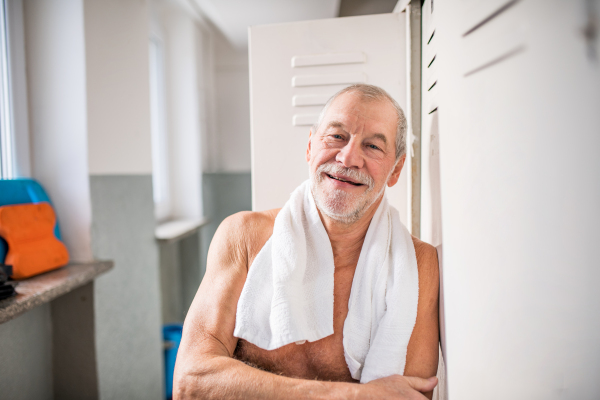 Senior man standing by the lockers in an indoor swimming pool. Active pensioner enjoying sport.