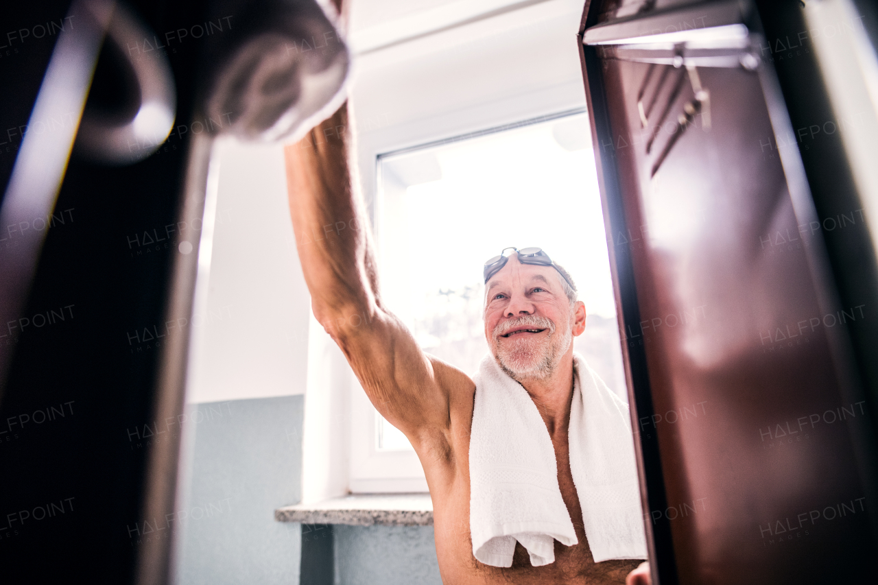 Senior man by the lockers in an indoor swimming pool. Active pensioner enjoying sport.