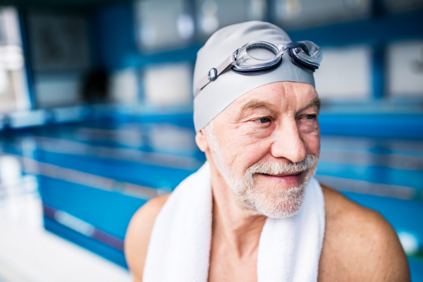 Senior man standing in an indoor swimming pool. Active pensioner enjoying sport.