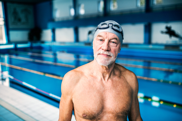 Senior man standing in an indoor swimming pool. Active pensioner enjoying sport.